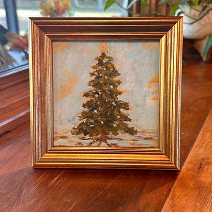 Framed painting of a Christmas tree on a wooden surface